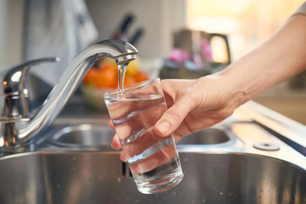 Glas water dat wordt gevuld onder een keukenkraan met kraanwaterfilter