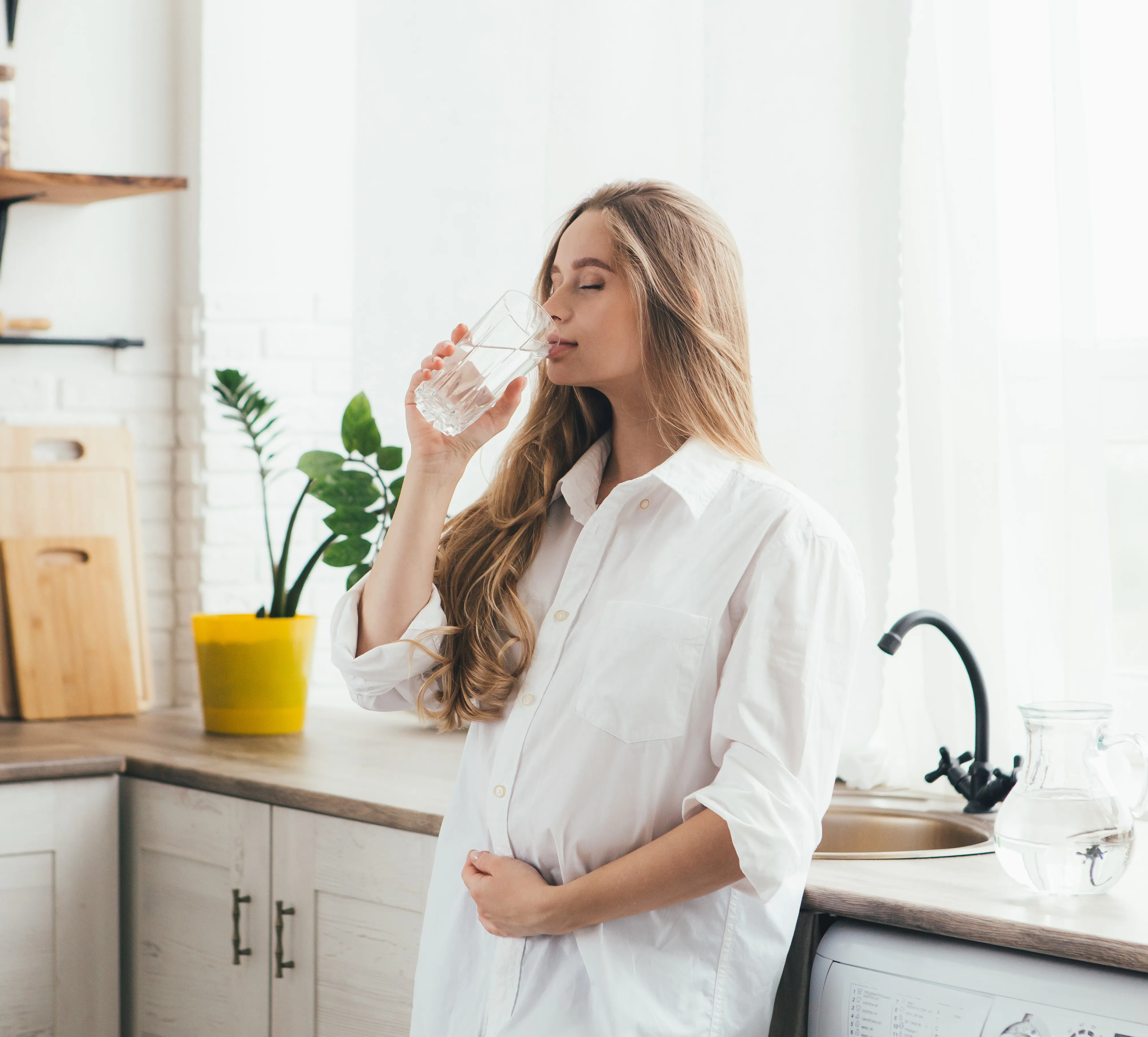 Vrouw tapt een glas gefilterd water uit de kraan in haar keuken