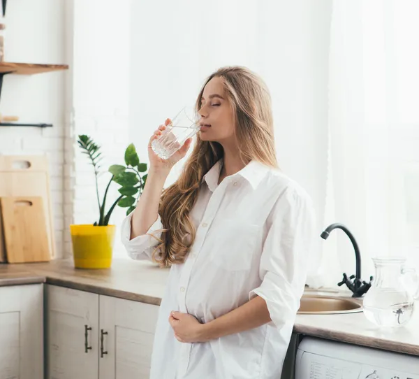 Vrouw drinkt schoon gefilterd kraanwater in de keuken