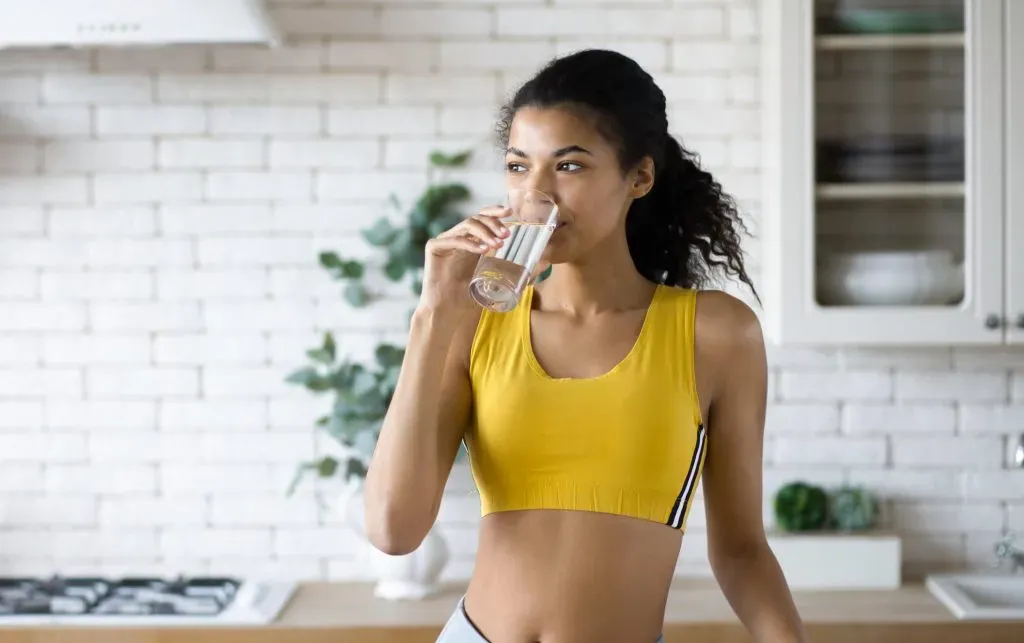 Vrouw drinkt een glas gefilterd kraanwater in een lichte keuken