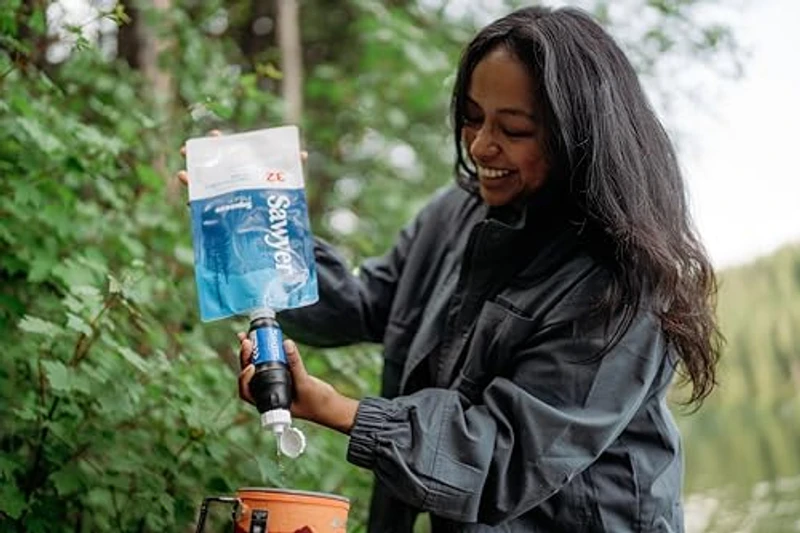 Vrouw knijpt water door Sawyer Squeeze filter in een beker tijdens het kamperen
